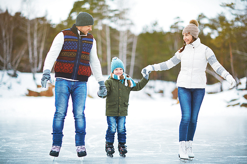 Young family holding hands and ice skating on rink