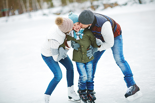 Happy parents kissing their cute son on skating rink