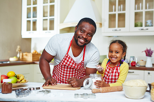 Cheerful man and cute little girl in aprons going to cook pastry