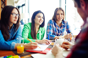 Young women talking to their male classmate in cafe