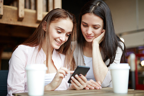 Happy girls reading promo sms while relaxing in cafe