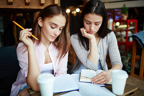 Two friendly girls reading book while preparing for lesson