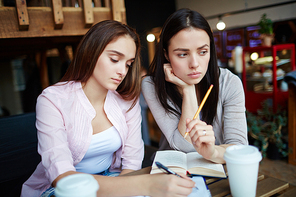 Pensive girls carrying out home assignment in cafe