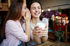 Cheerful girls gossiping while having drink in cafe