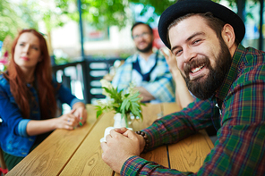 Friendly people sitting by table in cafe, happy bearded man 