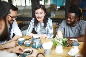 Intercultural young people chatting by cup of tea in summer cafe