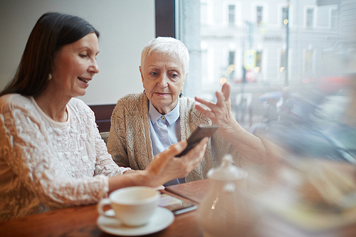 Two friendly senior women reading sms in smartphone of one of them