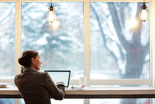 Businesswoman with laptop looking through window while spending time in cafe