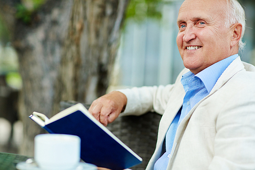 Happy senior man with open book or diary relaxing outdoors