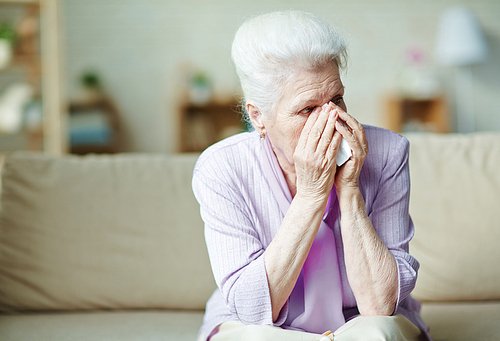 Crying elderly woman holding handkerchief by her face