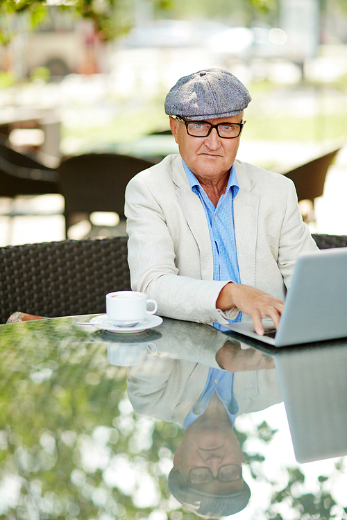 Senior man sitting at cafe and typing on laptop