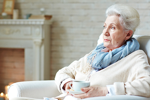 Calm female with cup of drink sitting in arm-chair