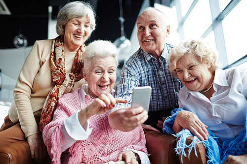 Group of friendly seniors with smartphone having fun in cafe