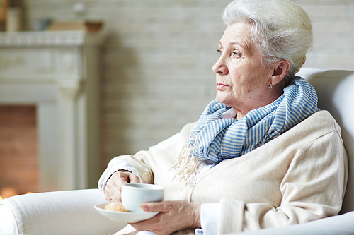 Calm elderly woman with cup of tea relaxing at home