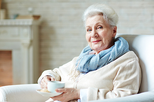 Senior female sitting in arm-chair with cup of tea and 
