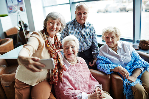 Group of carefree seniors with smartphone making selfie in cafe
