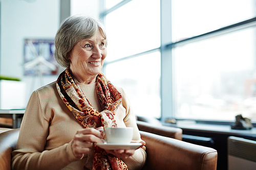 Smiling senior female with cup of tea looking through window