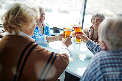 Group of friendly seniors toasting with beer in cafe