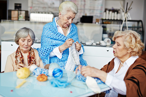 Group of elderly women knitting and talking by table