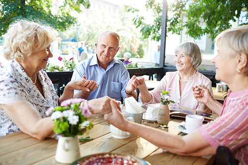 Group of friendly seniors holding by hands by table