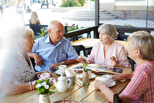 Aged woman showing her photo album to friends