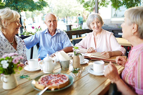 Friendly senior people having talk by table in cafe