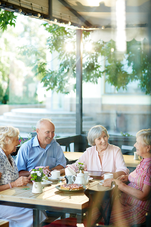 Happy seniors sitting by table and talking at leisure