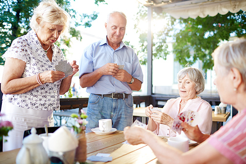 Restful seniors playing cards in outdoor cafe at leisure