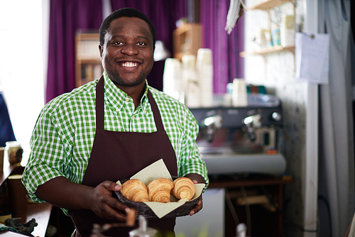Smiling baker holding plate with croissants
