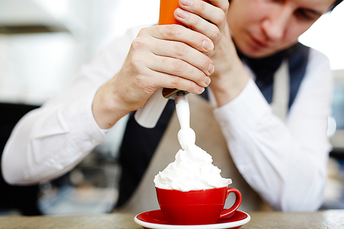 Barista decorating coffee with whipped cream