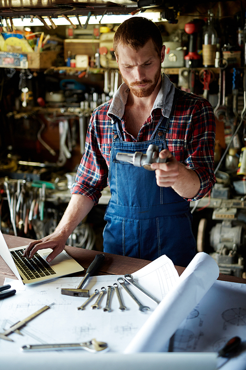 Modern engineer looking at metallic part in workshop