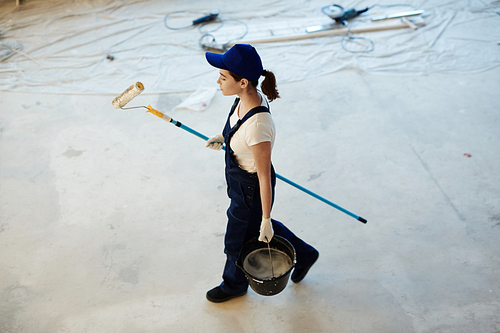Young female worker carrying paintroller and bucket with water