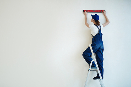 Woman in uniform keeping level tool close to painted wall