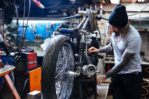 Man with tattoos repairing custom bike in workshop