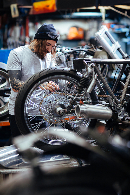 Hipster with tattoo repairing custom-bike in workshop