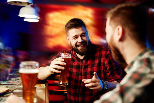 Happy young man with beer and his friend talking in the pub