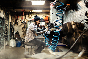 Biker sitting in his garage and repairing motor of custom-bike