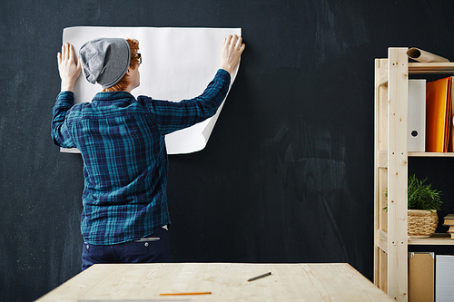 Young modern architect hanging paper onto blackboard