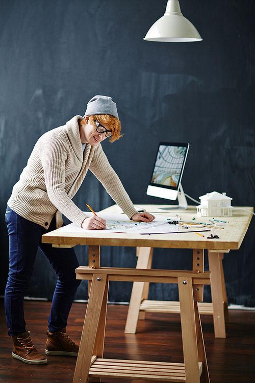 Young specialist drawing sketch while standing by table