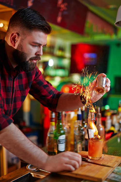 Young barman putting red hot pepper into burning cocktail