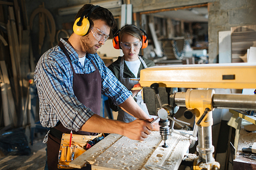 Carpenter in uniform and protective headphones working by drill machine