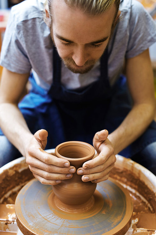 Young potter making clay jug in his workshop