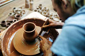 Self-employed potter using special tool while making clay item