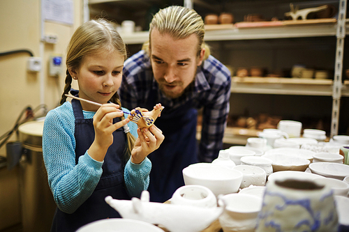 Adorable girl painting clay bird with her father near by