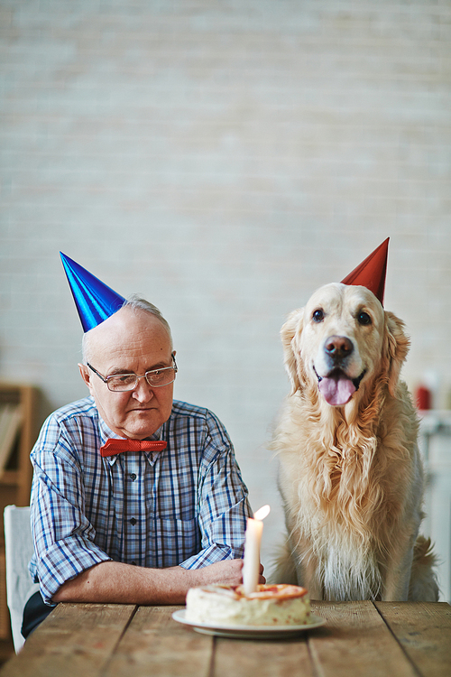 Mature man and his pet sitting by table with birthday cake with burning candle