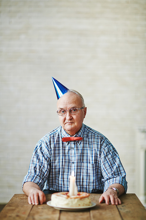 Mature man sitting by table with birthday cake and 