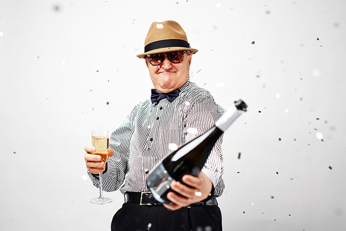 Man in sunglasses and hat holding champagne bottle and toasting with flute