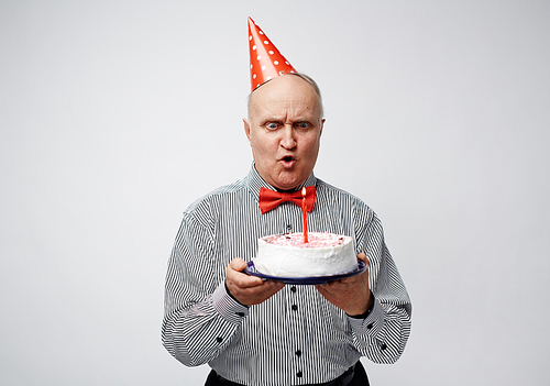 Indignant senior man looking at burning candle on birthday cake