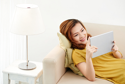 Young Asian woman relaxing on sofa with digital tablet