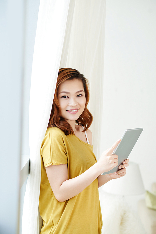 Portrait of Vietnamese young woman with digital tablet standing at home